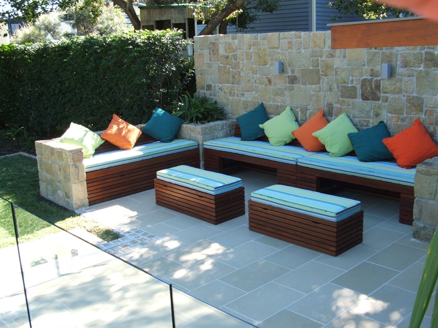 L-shaped Kwila bench seating with cushions and two mobile ottomans beside a pool